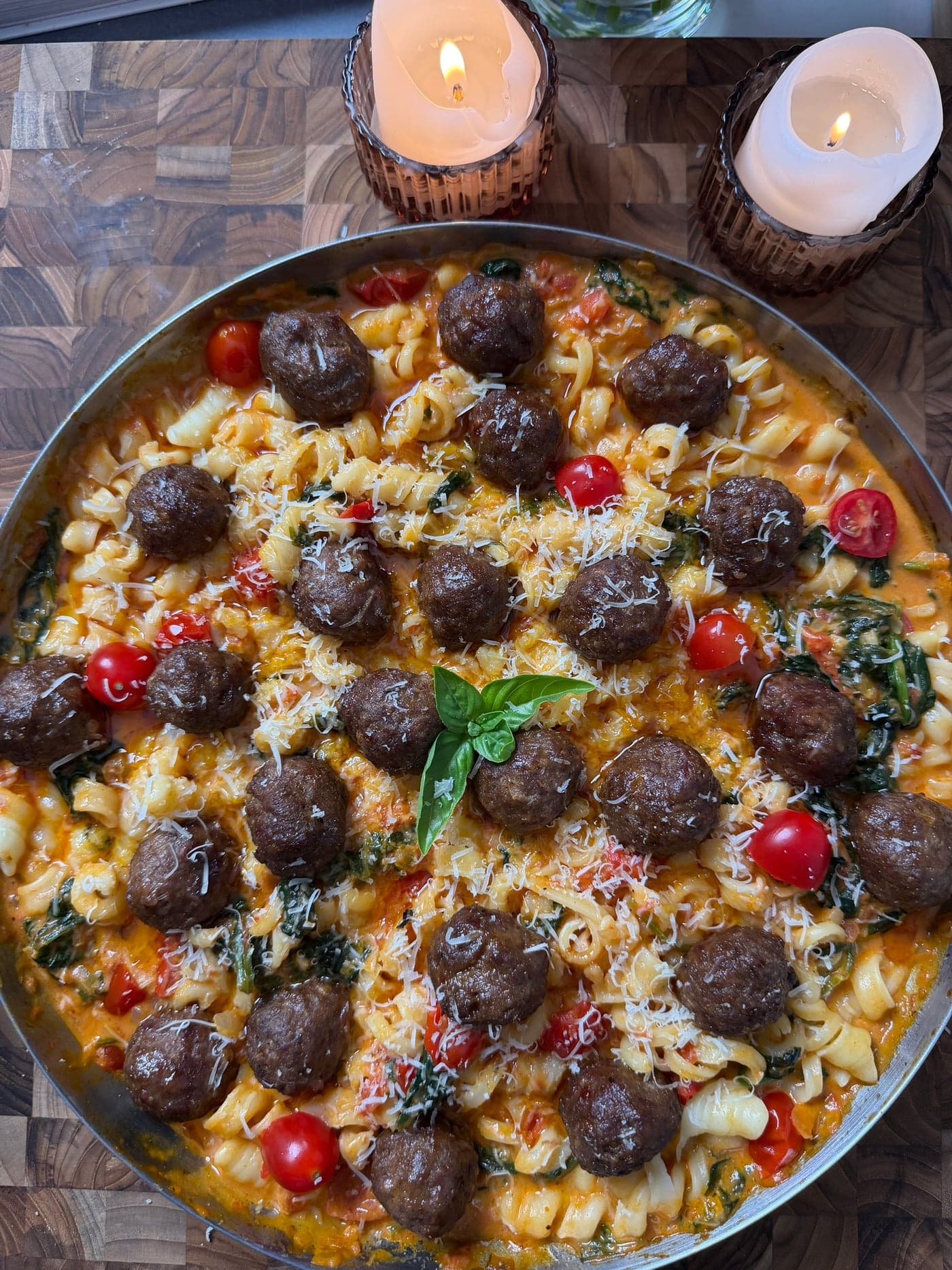 Skillet of creamy tomato and spinach pasta with meatballs, cherry tomatoes, grated Parmesan and fresh basil
